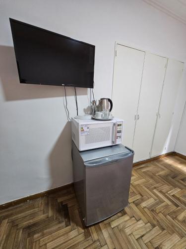 a microwave sitting on a stand with a television on a wall at habitacion comoda cerca del obelisco in Buenos Aires