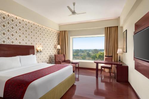 ein Hotelzimmer mit einem Bett und einem großen Fenster in der Unterkunft Ramada by Wyndham Jaipur Jaisinghpura in Jaipur