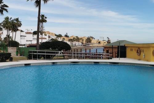 a large blue swimming pool with palm trees and buildings at Estudio reformado primera linea playa in Sitio de Calahonda