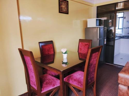 a dining room table with pink chairs and a refrigerator at COMODORO DEPARTAMENTOS in Oruro