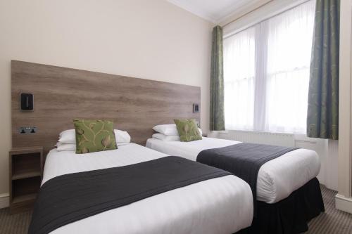 a hotel room with two beds and a window at Kensington Gardens Hotel in London