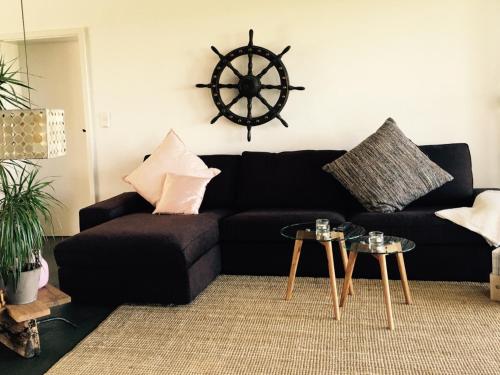 una sala de estar con un sofá negro y una rueda de barco en la pared en Beltblick, en Fehmarn