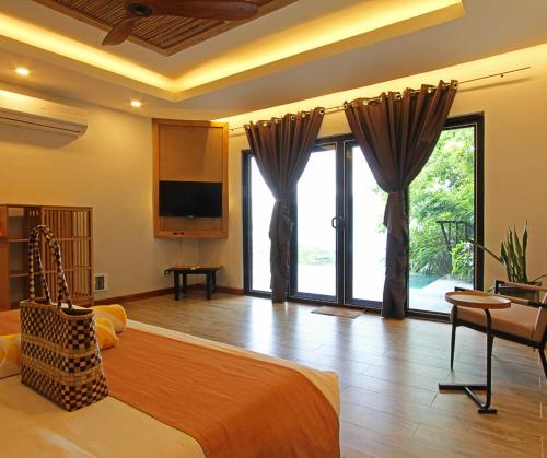 a bedroom with a large bed with a television and sliding glass doors at Bugana Beach and Dive Resort in Manlocahoc