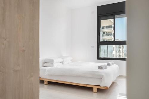 a white bedroom with a bed and a window at Luxury Flat with Balcony & Ocean View by torohome in Ashdod