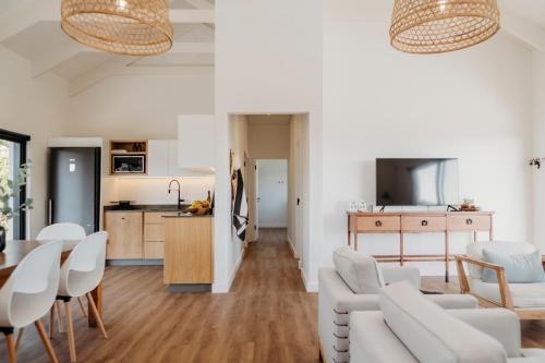 a living room and kitchen with white chairs and a table at Uitwaaien Beach Cottage in Pearly Beach
