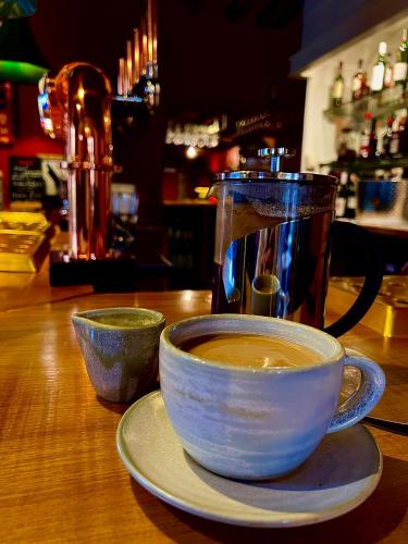 a cup of coffee sitting on a table with a tea pot at Five Alls in Lechlade