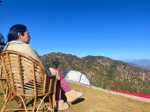 a man sitting in a chair looking at the mountains at Maayaa Ridge House in Kanatal