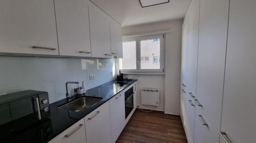 eine Küche mit weißen Schränken, einem Waschbecken und einem Fenster in der Unterkunft Apartment Heidi in Spiez