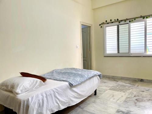 a white bedroom with a bed and a window at sai bliss in Puttaparthi