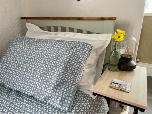 a bed with a pillow and a table with a vase on it at Seaside Homestay - Ensuite twin room with Kitchenette in Paignton