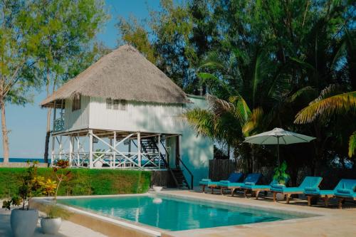 a swimming pool with chairs and an umbrella and a building at Villa Passiflora Zanzibar in Jambiani