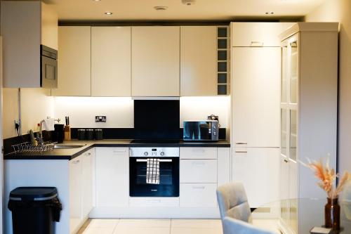 Stunning Ground Floor Apartment for Business & Leisure Stays in RG2 - Sleeps up to 6! في ريدينغ: مطبخ مع دواليب بيضاء وطاولة زجاجية