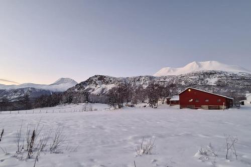 a red barn in a snow covered field with mountains at Flott leilighet midt blant Lyngsalpene! in Lyngseidet
