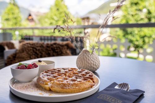 a plate with a waffle and a bowl of fruit on a table at Quality Hosts Arlberg - Hotel ANTON in Sankt Anton am Arlberg