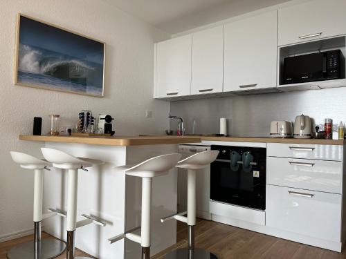 une cuisine avec des placards blancs et des tabourets de bar blancs dans l'établissement PREMIERE LIGNE OCEAN APPART STANDING 50M2 2 Chambres, à Lacanau