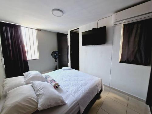 een slaapkamer met een bed met witte lakens en een televisie bij Caobos 1212 in Girón