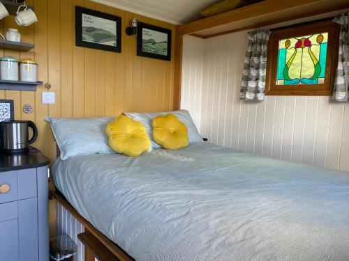 a bed with two yellow pillows in a room at Shepherds Hut in the Hills - Nr. Mold in Nannerch