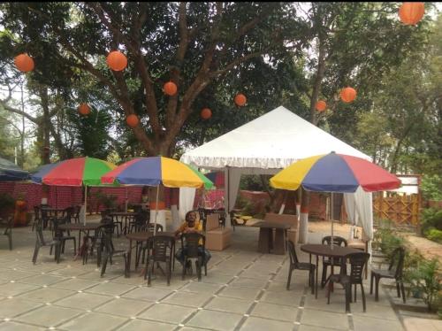 eine Gruppe von Tischen und Stühlen mit bunten Sonnenschirmen in der Unterkunft Basundhara Resort Cum Family Restaurant in Kharagpur