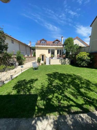 une cour verdoyante avec une maison et une chaise dans l'établissement Maison lumineuse avec jardin, proche Paris Disney et Paris, à Lagny-sur-Marne
