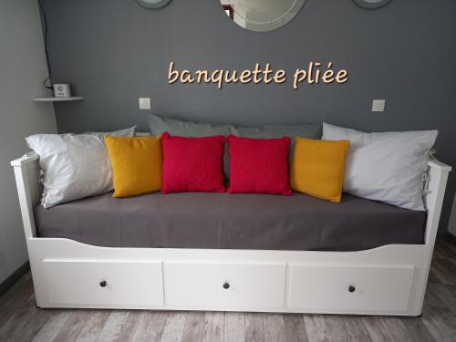 a white bed with four colorful pillows on it at Studio "l'aube du Perche" in La Mancelière