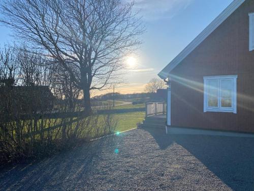 a house with the sun setting behind a tree at Stort semesterhus med sol in Båstad