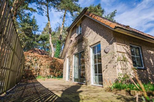 uma casa de tijolos com uma cerca em frente em Wellnesshuis met jacuzzi en sauna in het bos em Lunteren