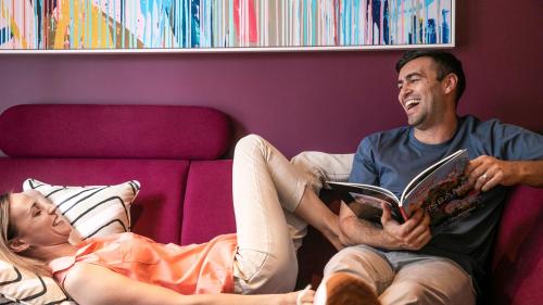 Ein Mann und eine Frau sitzen auf einer Couch und lesen ein Buch in der Unterkunft Hotel Indigo Brisbane City Centre, an IHG Hotel in Brisbane