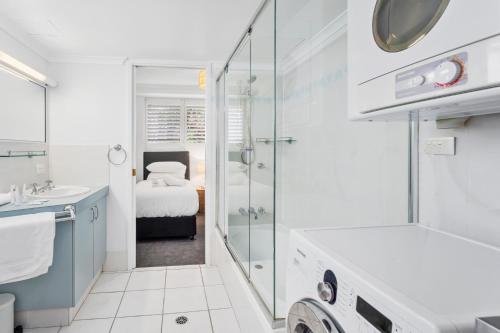 a white bathroom with a shower and a sink at Beachfront 2-Bed with Pool, BBQ & Tennis Court in Gold Coast