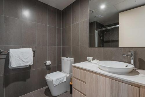 ein Badezimmer mit einem Waschbecken, einem WC und einem Spiegel in der Unterkunft Lonsdale St 1-Bed Unit with Study Area and Parking in Canberra