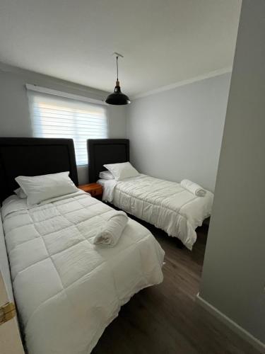 una camera con due letti con lenzuola bianche e una finestra di Casa amoblada en sector residencial a Vallenar