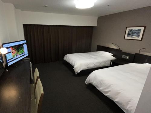 a hotel room with two beds and a flat screen tv at Hotel Alpha-One Himeji Minamiguchi in Himeji