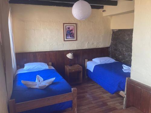 a bedroom with two beds with blue sheets and a lamp at Samay Wasi Hostel in Cusco