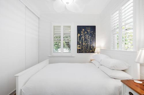 a white bedroom with a white bed and windows at Tranquil 2-Bed Family Home with Deck Among Trees in Brisbane