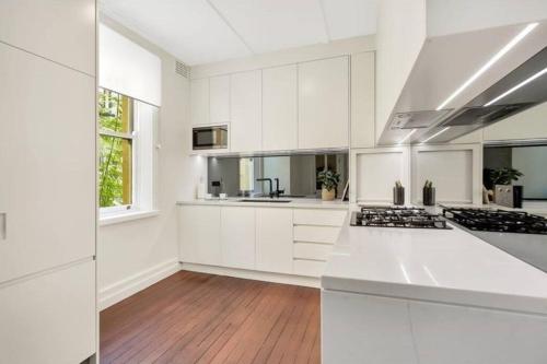 a white kitchen with white cabinets and a hardwood floor at Chic Large 4 Bedroom Barangaroo The Rocks Sydney in Sydney