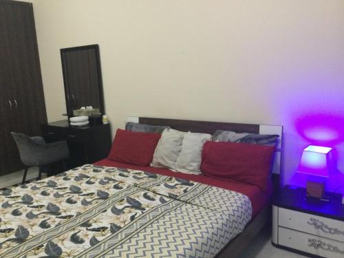 - une chambre avec un lit doté d'oreillers rouges et d'une lampe violette dans l'établissement 1 bedroom apartment, à Fujaïrah