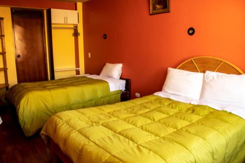 two beds in a hotel room with orange walls at PUNO ANDENES Suite in Puno