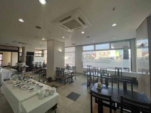 un comedor con mesas y sillas blancas y ventanas en Hotel Alpha-One Tsuruoka en Tsuruoka