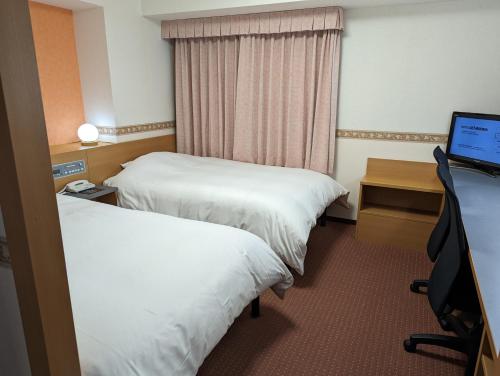横浜市にあるホテルアルファーワン横浜関内のベッド2台、デスク、コンピュータが備わるホテルルームです。