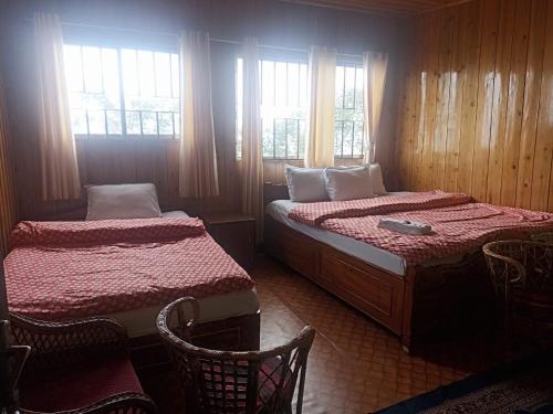 a bedroom with two beds and two chairs and windows at HOTEL NIRALA , Darjeeling in Darjeeling