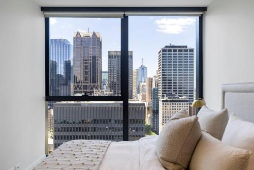 una camera da letto con una grande finestra con vista sulla città di Luxuria Apartments - Collins House a Melbourne