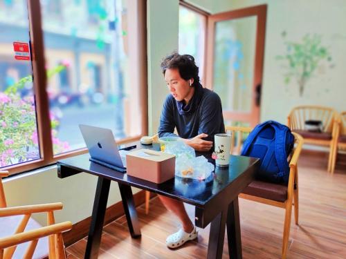 a woman sitting at a table with a laptop at Sea Sunset Hotel Phu Quoc - Welcome to a mixing world of friends in Phu Quoc