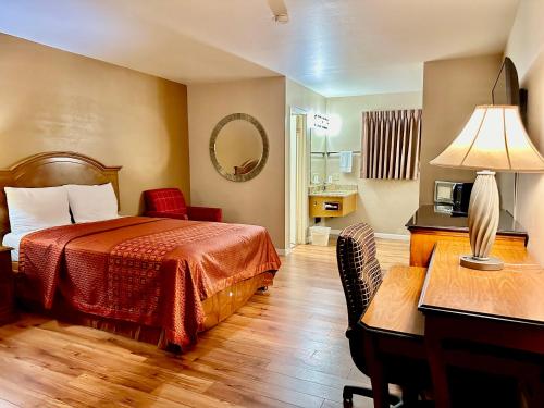 Habitación de hotel con cama y escritorio con lámpara. en Franciscan Inn Motel en Vista