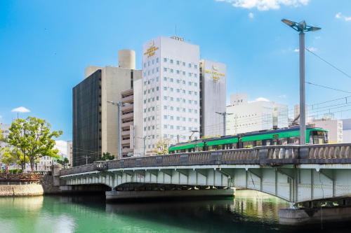 un train sur un pont sur une rivière avec des bâtiments dans l'établissement Hiroshima Intelligent Hotel Annex, à Hiroshima