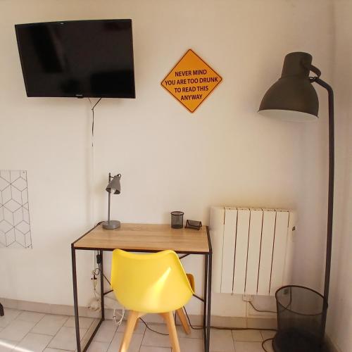 un bureau avec une chaise jaune et une télévision murale dans l'établissement le dhuoda climatisé, à Nîmes