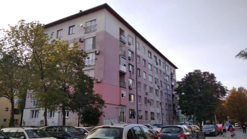 a pink building with cars parked in a parking lot at Apartman Kvart in Sarajevo