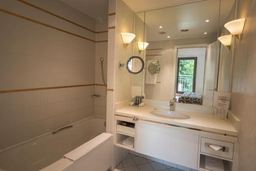 La salle de bains est pourvue d'une baignoire, d'un lavabo et d'un miroir. dans l'établissement Hotel Parc Belair, à Luxembourg