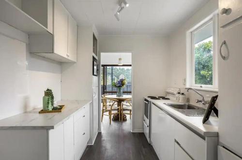 a white kitchen with a sink and a table at Cozy 3BR West Auckland in Auckland