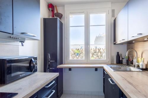 a kitchen with blue cabinets and a large window at Joli 2 pièces avec balcon. in Boulogne-Billancourt