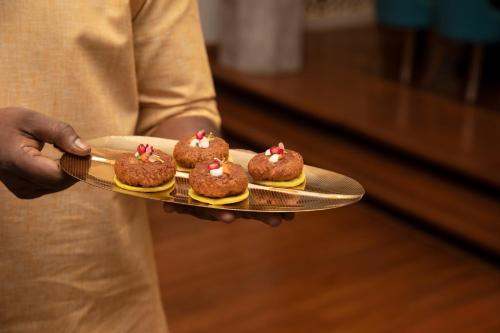 a person holding a tray with four cupcakes on it at The Westin Mumbai Powai Lake in Mumbai