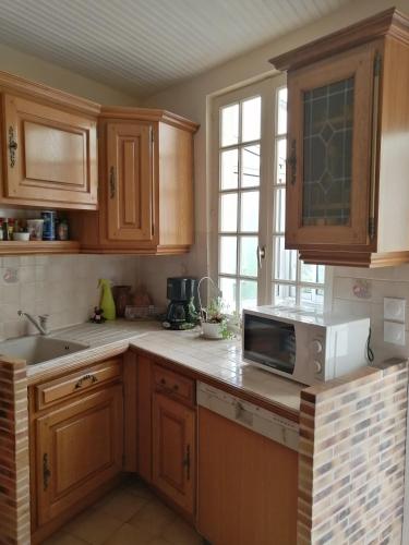 La cuisine est équipée de placards en bois, d'un évier et d'un four micro-ondes. dans l'établissement maison entre terre et mer, à Bonnebosq